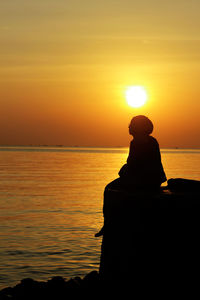 Silhouette woman sitting at beach during sunset