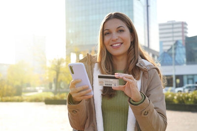 Girl typing number of credit card on smartphone makes purchase online looking at camera