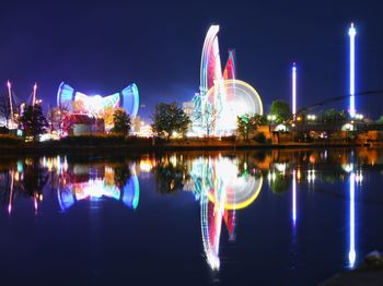 Illuminated buildings by river against sky at night