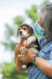 Senior woman wearing mask holding puppies standing outdoors