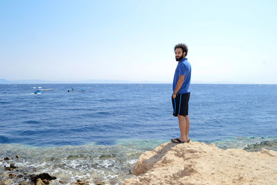 Portrait of young man standing at beach against sky