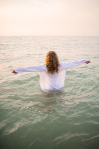 Happy young woman wear white shirt standing in sea water over sun set outdoors. 