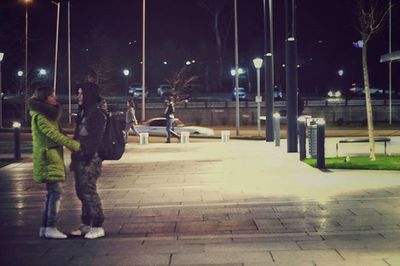 Rear view of woman standing on illuminated street at night