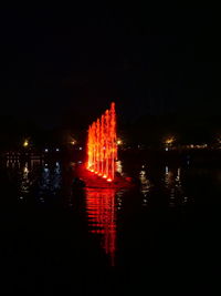 Illuminated buildings by lake against sky in city at night