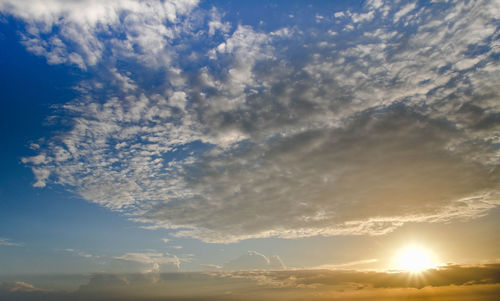 Low angle view of sunlight streaming through clouds during sunset