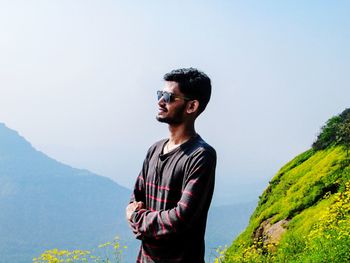 Young man wearing sunglasses standing against mountain range