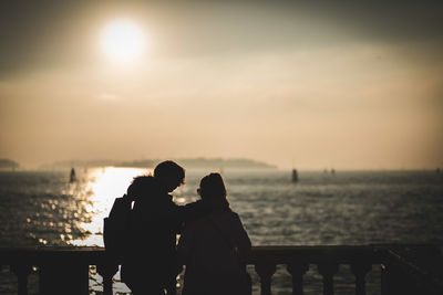 Rear view of couple standing against sky during sunset