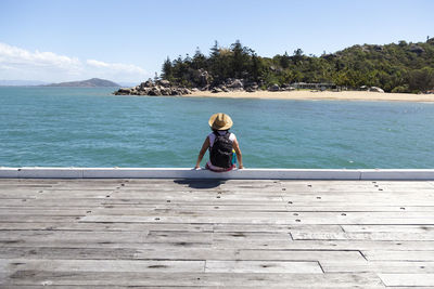 Rear view of woman sitting on sea against sky