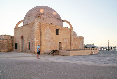 Man walking in front of historical building against clear sky