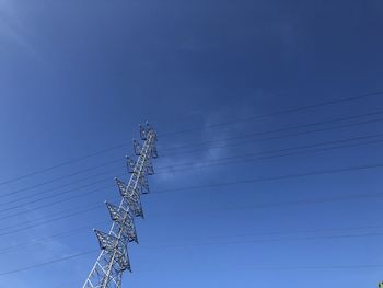 Low angle view of electricity pylon against blue sky