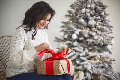 Side view of woman using laptop while sitting on christmas tree