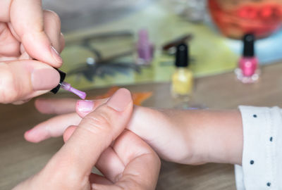 Cropped hands applying nail polish on girl fingernail