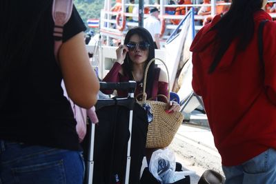 Portrait of woman wearing sunglasses with luggage standing at harbor