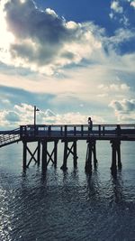 Silhouette teenage boy standing on pier over sea against cloudy sky