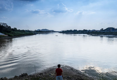 Rear view of man standing on shore against sky