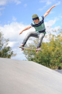 Boy skateboarding in mid-air against sky