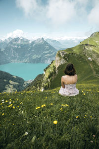 Rear view of woman sitting on grass against mountains and sky