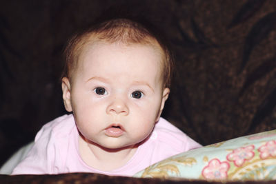 Close-up portrait of cute baby girl relaxing on sofa in darkroom