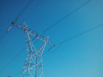 Low angle view of electricity pylon against clear blue sky