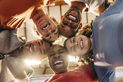 Happy male and female athletes laughing while huddling together at sports court