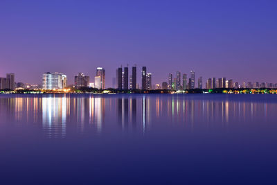 Sea by illuminated buildings against clear sky at night