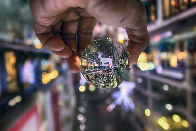 Close-up of human hand holding crystal ball against illuminated lighting equipment at night