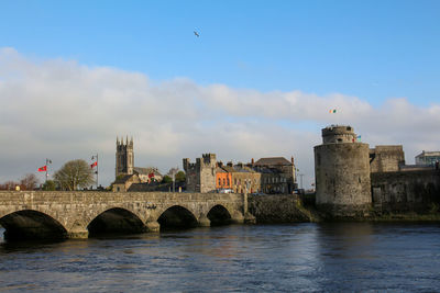 Arch bridge over river by buildings against sky