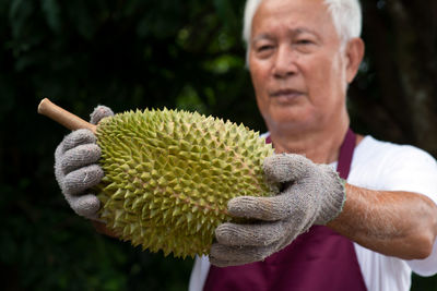 Midsection of man holding durian while standing against trees