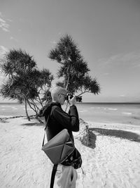 Rear view of woman sitting on beach against sky