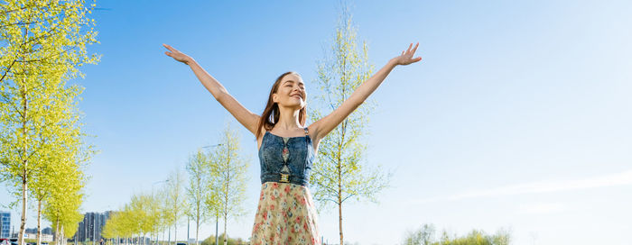 Low angle view of woman with arms raised standing on field against sky