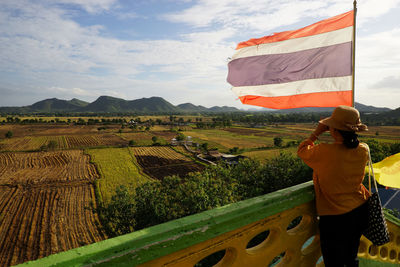 Rear view of woman standing by railing and flag against sky