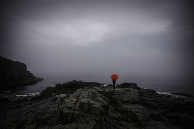 Person standing on rock formations by sea against sky