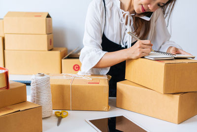 Midsection of woman writing in note pad on boxes