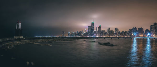 Illuminated cityscape by sea against sky at night