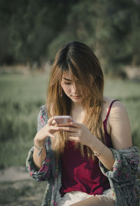 Young woman using mobile phone against trees