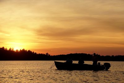 Silhouette people in boat on sea against sunset sky