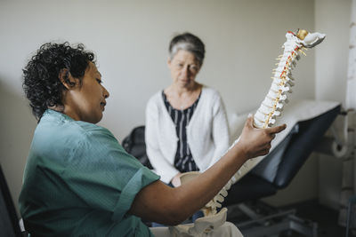 Doctor explaining senior patient over spine model in clinic