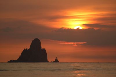 Silhouette rock formation in sea against orange sky