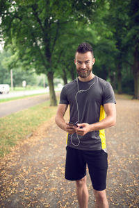 Portrait of smiling athlete listening to music through mobile phone in park