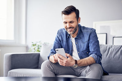 Smiling man sitting on sofa using cell phone
