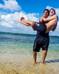 Full length of happy friends standing on beach against sky