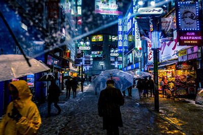 Rear view of people walking on illuminated street at night