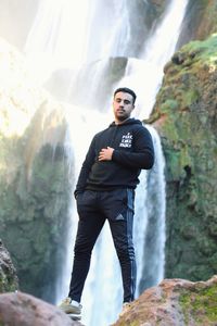 Portrait of young man standing against waterfall