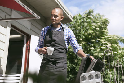 Man having coffee while standing by serving trays outside cafe