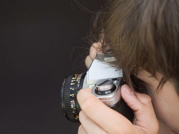 Close-up of boy photographing through camera against black background
