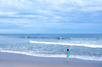 Rear view of girl walking on beach against sky