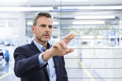 Businessman looking at graph on glass pane in factory hall