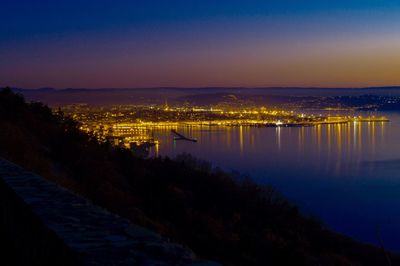 High angle view of illuminated city by river against sky at sunset