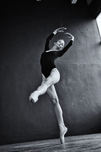 A ballerina in a bodysuit and pointe shoes moves around the room with long strides