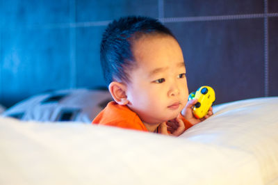 Cute boy looking away while holding toy on bed at home